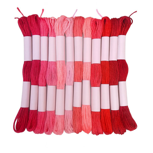 Madejas de hilo Mouliné en tonos rojos, rosados y coral dispuestas en fila con etiquetas blancas sobre fondo blanco, ideales para bordado y proyectos creativos.