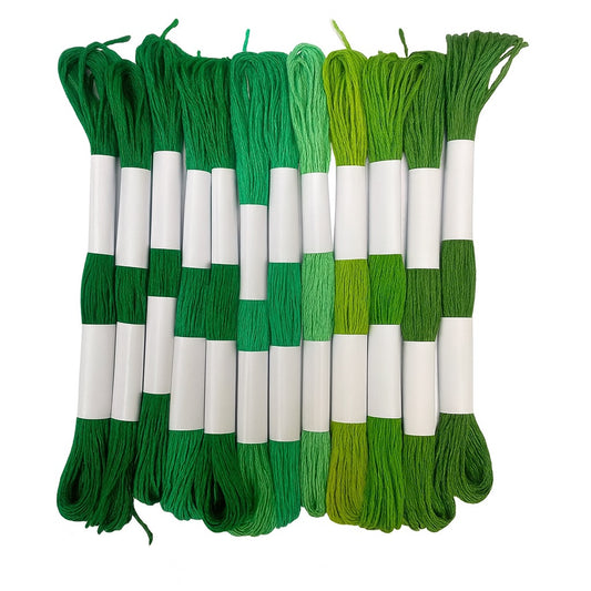 Madejas de hilo Mouliné en tonos verdes, desde verde oscuro hasta verde lima, dispuestas en fila con etiquetas blancas sobre fondo blanco.