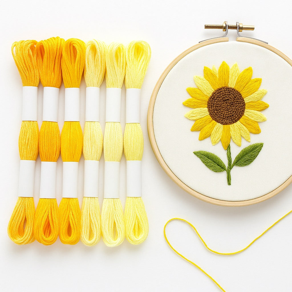 Madejas de hilo Mouliné en tonos amarillos junto a un bastidor con bordado moderno de girasol en degradado de amarillos sobre fondo blanco.