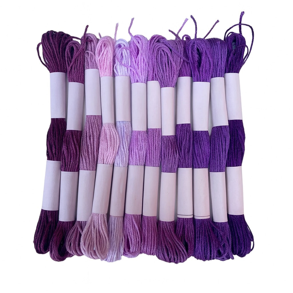 Madejas de hilo Mouliné en tonos morados y lilas dispuestas en fila con etiquetas blancas sobre fondo blanco, ideales para bordado y manualidades creativas.