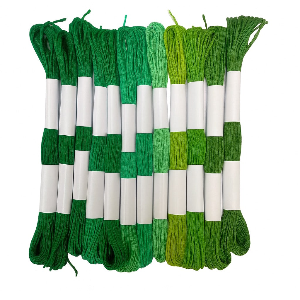 Madejas de hilo Mouliné en tonos verdes, desde verde oscuro hasta verde lima, dispuestas en fila con etiquetas blancas sobre fondo blanco.